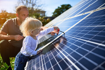 Man showing his small child the solar panels during sunny day. Father presenting to son modern...