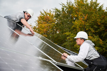 Technicians building photovoltaic solar module station on roof of house. Men electricians in...