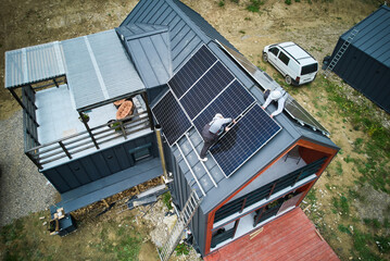 Electricians connecting cables while installing photovoltaic solar panels on roof of house. Aerial view of mounters mounting of PV solar module on rooftop. Concept of alternative and renewable energy.