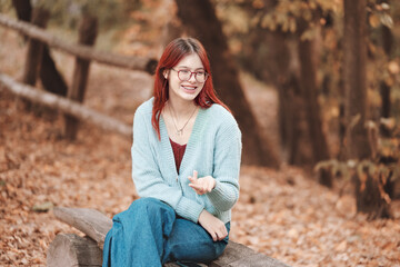 Red-haired girl in a blue sweater communicates by gesturing with her hands. Bench in an autumn park, yellow foliage.