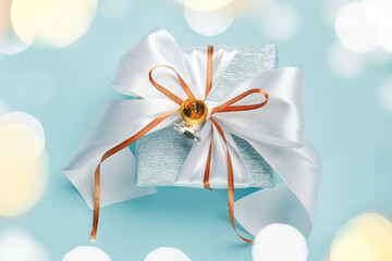 Gift box wrapped in blue silver paper with white and gold ribbon bow. Blue background, bokeh light, top view. Christmas and New Year gifts, Boxing Day.