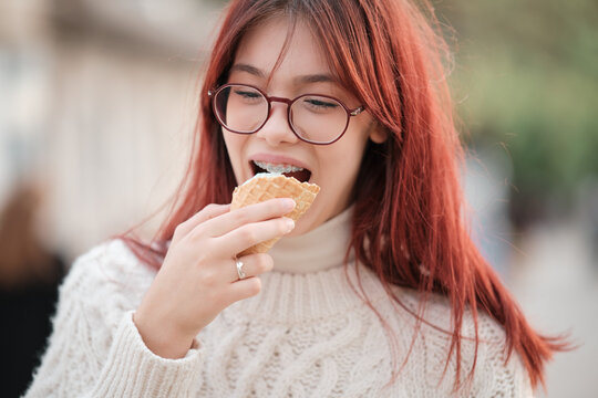 Girl in a white sweater eats ice cream in a waffle cone.