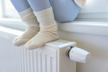 Feet of little girl in warm white socks. Child sitting and warming up from the heating radiator....
