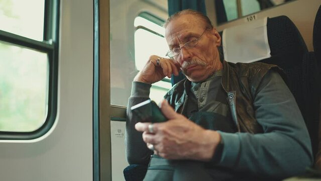 Pensive senior uses mobile phone while traveling in train coupe