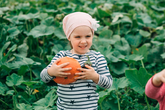 Smiling girl wearing bandana and holding pumpkin in vegetable garden