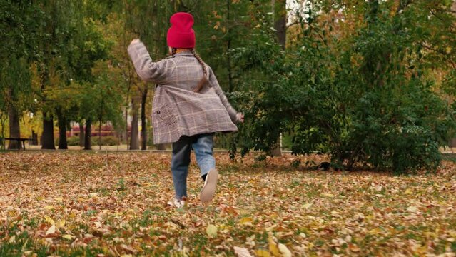 Funny little girl runs along lawn with yellow leaves in autumn city park