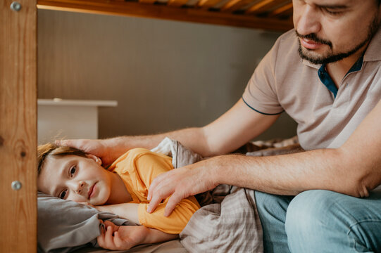 Boy lying on bed with father caressing him at home