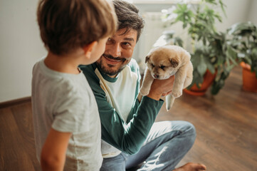 Smiling man showing cute puppy to son at home