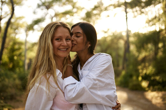Teenage girl kissing happy mother in forest at sunset