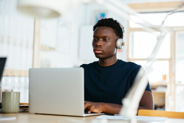 Young student with wireless headphones using laptop at university