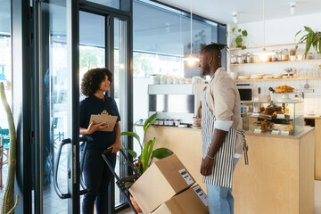 Waiter standing near box container and talking to delivery woman in cafe