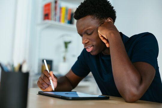 Young Student Studying And Writing On Tablet PC At Desk