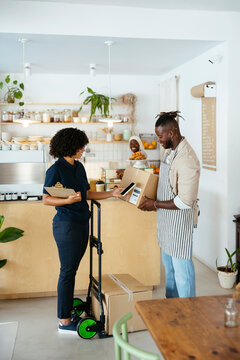 Waiter carrying box container and delivery woman scanning QR code in cafe