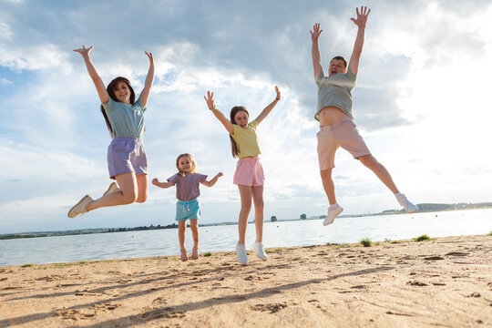 Cheerful parents with daughters jumping at beach - Powered by Adobe