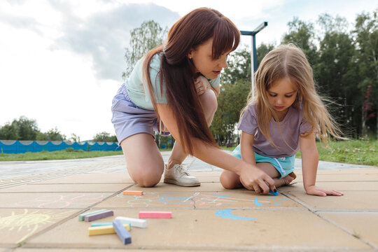 Woman teaching daughter to draw with chalk on tiled floor at park