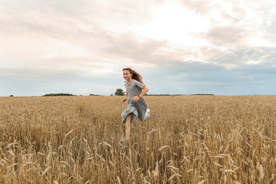 Happy girl running amidst field under sky