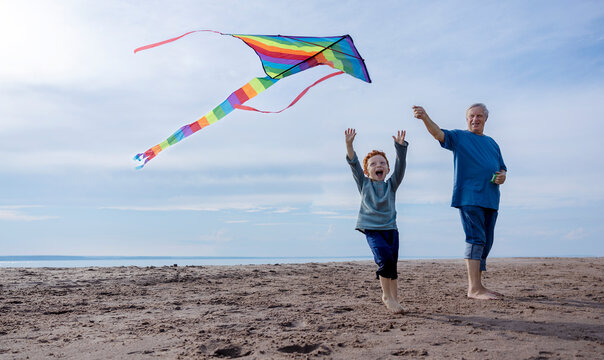 Happy boy flying multi colored kite with grandfather at beach