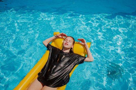 Girl with eyes closed relaxing on pool raft at sunny day