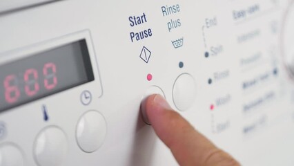 Close up shot of slow motion finger pressing start pause button on washing machine dial rinse clothing cleaning laundry detergent household 4K