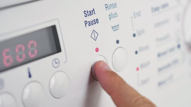 Close up shot of slow motion finger pressing start pause button on washing machine dial rinse clothing cleaning laundry detergent household 4K