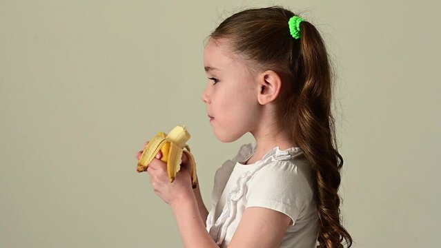 Happy little girl bites and eats banana, fruit and baby.