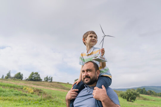 Father carrying son on shoulders with wind turbine model in front of sky