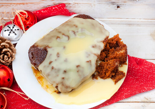 Traditional South African Malva pudding with creamy custard on rustic Christmas table. A favorite dessert all year round.