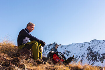 Contemplative man sitting with backpack on mountain in winter