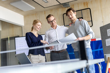 Smiling businessman discussing over document with colleagues in modern office
