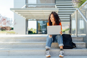 Smiling student sitting with laptop on steps in campus