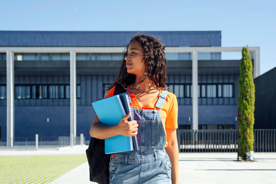 Student holding spiral notebooks and walking in front of building