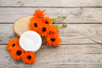 Fresh orange calendula flowers on a wooden background in nature. Cosmetic cream for cleansing the...