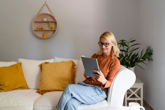Smiling mature woman with eyeglasses using tablet PC in living room at home