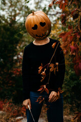 A girl in a Halloween pumpkin peeks out from behind the red leaves