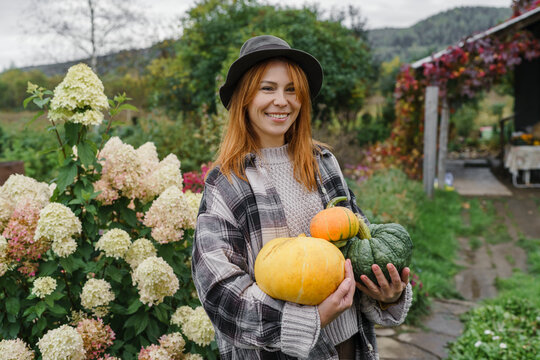 Happy farmer wearing hat holding pumpkins at farm