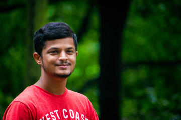"Dandeli, India- 6th december 2022:Portrait of young Indian man in red shirt on green nature background"