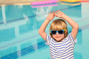 Preschooler, 4 year old boy enjoys holidays and summer time. Portrait of a child against the backdrop of a swimming pool. Kid in sunglasses and a striped T-shirt.