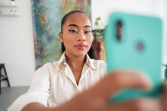 Soft focus of young Asian female employee taking selfie on cellphone for social media during break from work in modern office