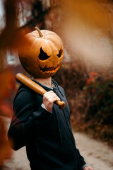 A man with a pumpkin on his head holds a bat and smiles ominously