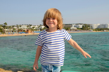 A cute boy enjoys the sea, in the background there is the coast and beaches, the beautiful color of the sea. Family trip to Cyprus. Vacation with children. Tourists on the island