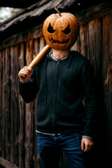A man with a pumpkin on his head holds a bat and smiles ominously