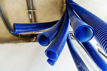 Large, corrugated plastic pipes for safe electrical wiring hang from the ceiling of an unfinished house. Foreground. Bottom up view - obrazy, fototapety, plakaty