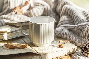 Autumn composition with a textured cup and a book on the windowsill.