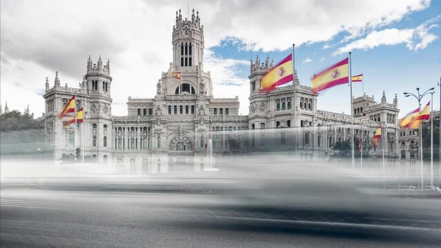 Timelapse at statue in the Plaza de Cibeles with the representation of the goddess of the same name and two lions with Spanish flags waving in the wind behind and traffic passing by