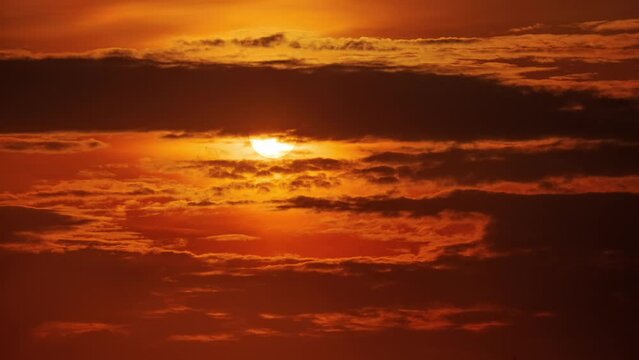 Sunset sun moving behind dark clouds in orange sky. Timelapse, 4K