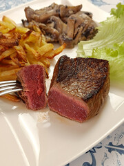 morceau de boeuf grillé dans une assiette accompagné de frites et champignons à la crème