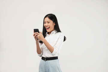 The photo of Surprised young Asian lady using mobile phone with positive expression, smiles broadly, dressed in casual clothing. Isolated on a white background. 