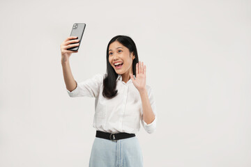 Smiling adorable young Asian female taking a selfie photo on her smartphone with a positive expression looking at the camera. 