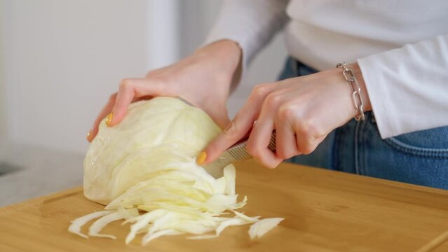 Young woman hands cutting cabbage head with sharp knife on wooden chopping board on table in domestic kitchen. Natural organic soup ingredient. Preparing vegetables for vegetarian dish. Food Delivery