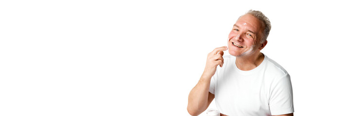 Banner. Portrait of middle aged, 45s man applying skin care cream on face against white background.